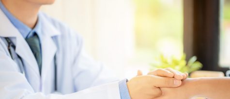 Friendly man doctor's hands holding male patient's hand for enco